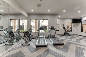 A spacious gym with treadmills, elliptical machines, and a television.